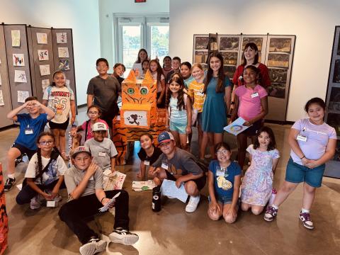 A group of students posting in front of a paper mache tiger in an art gallery.