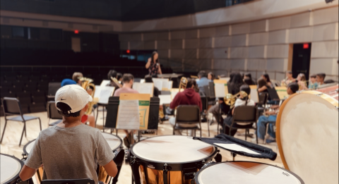 Students playing in a band on stage with the conductor in the front.