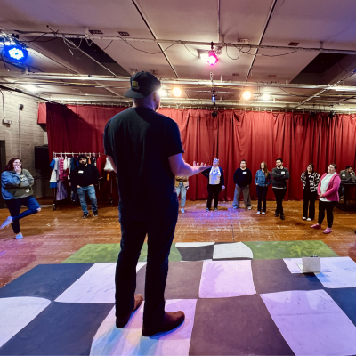 A teacher standing on a black and white checkered stage speaking to other teachers